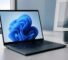 Laptop displaying the Windows 11 bloom wallpaper on a bright desk — choosing a Windows 11 edition