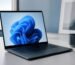 Laptop displaying the Windows 11 bloom wallpaper on a bright desk — choosing a Windows 11 edition